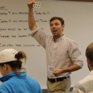 Andrew Bennett holding a playing card and showing it to the class in front of a white board